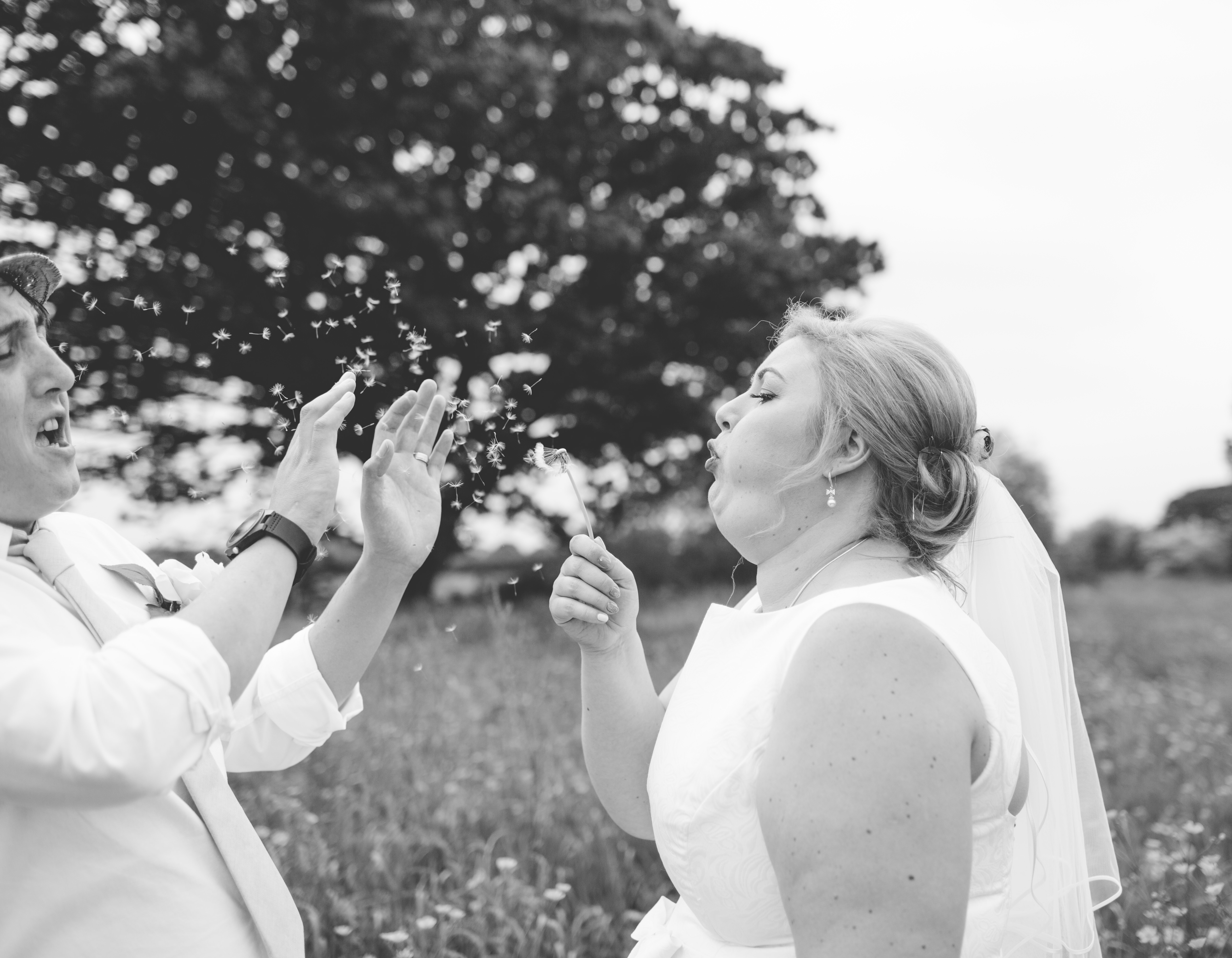 black and white photo of bride blowing dandelion at husband
