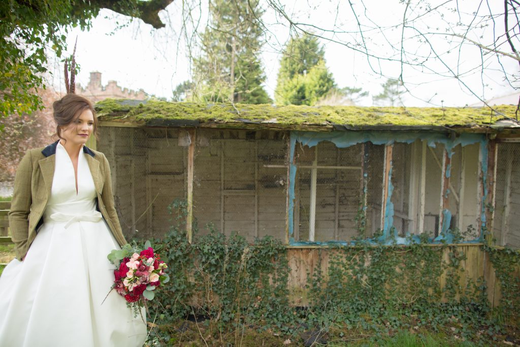 Bride stood holding bouquet next to old shed