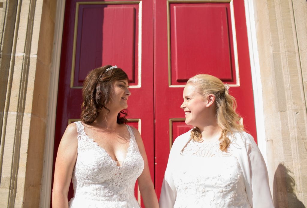 two brides stand outside red door at windsor guildhall