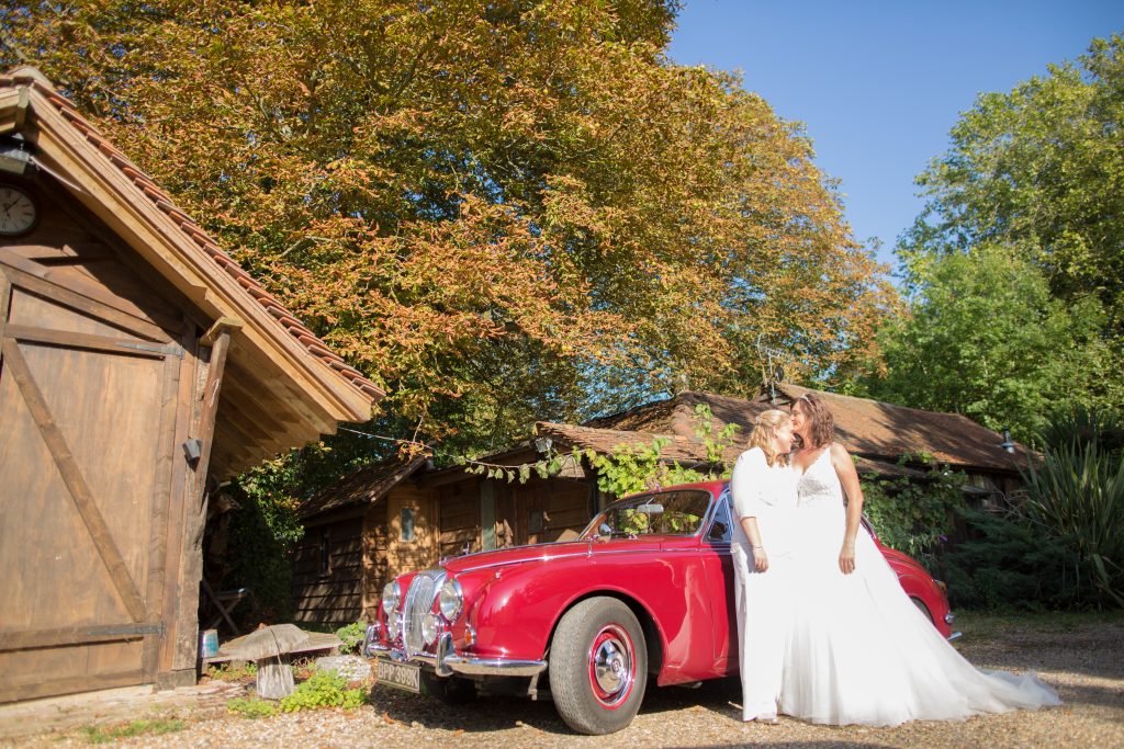 two brides standing in front of classic wedding car