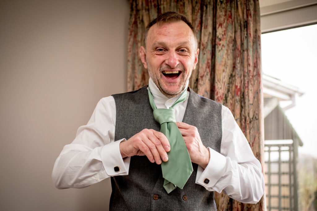 A man laughing on his wedding day trying to tie his tie!