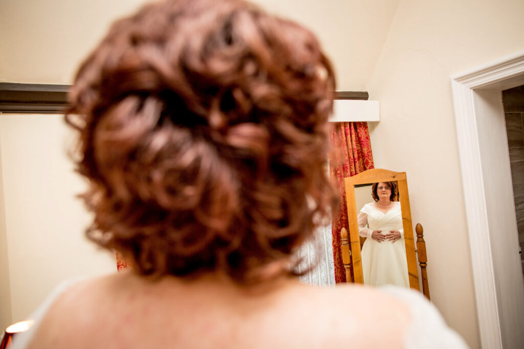 a bride in her wedding dress looking nervous in front of a full length mirror