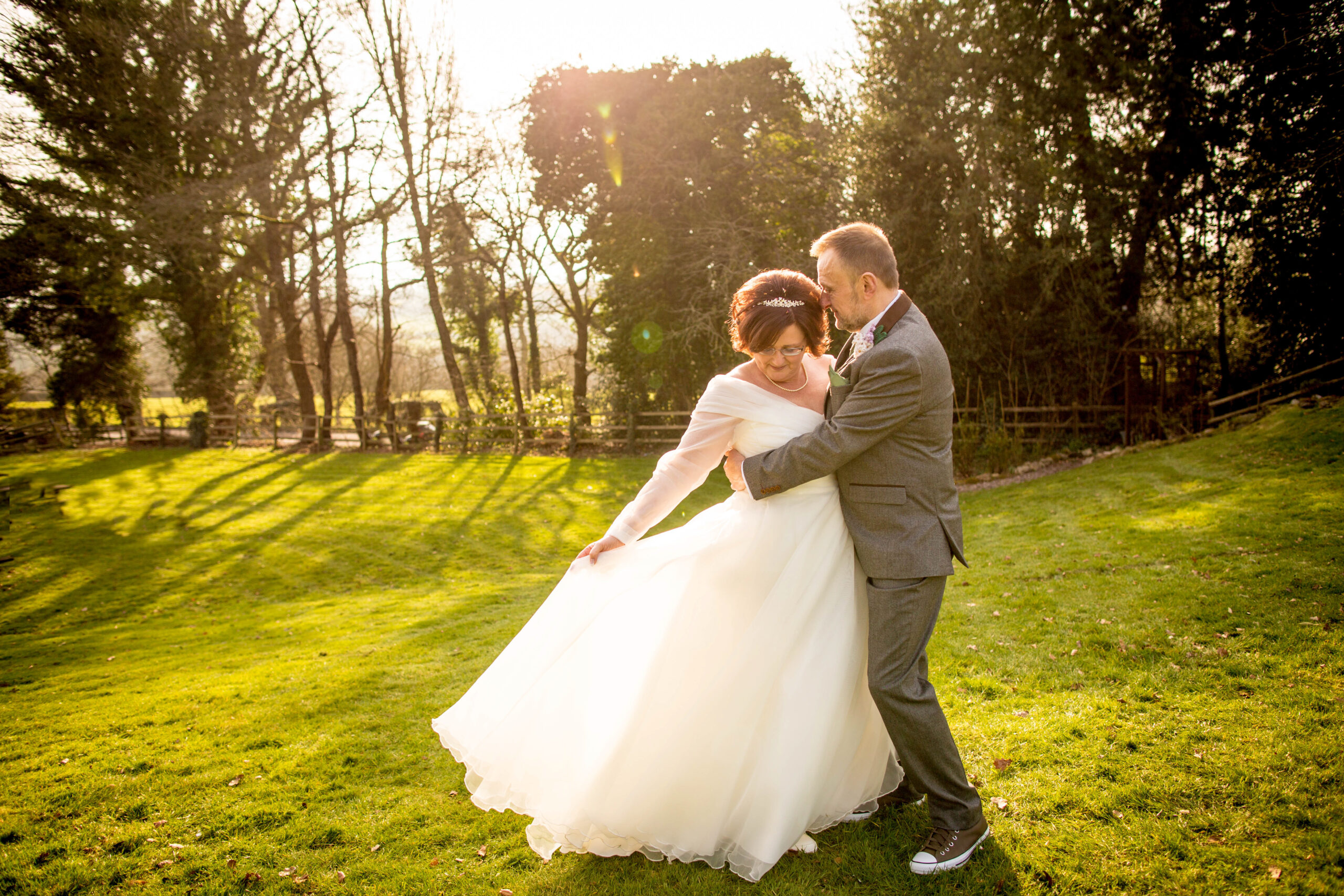 Image of a bride and groom stood outside bride is holding her dress out with one hand
