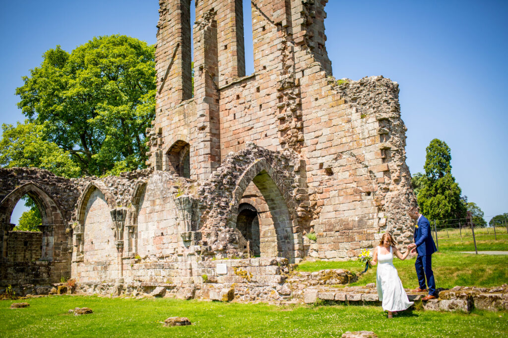 groom leading bride by hand as they walk through croxden abbey